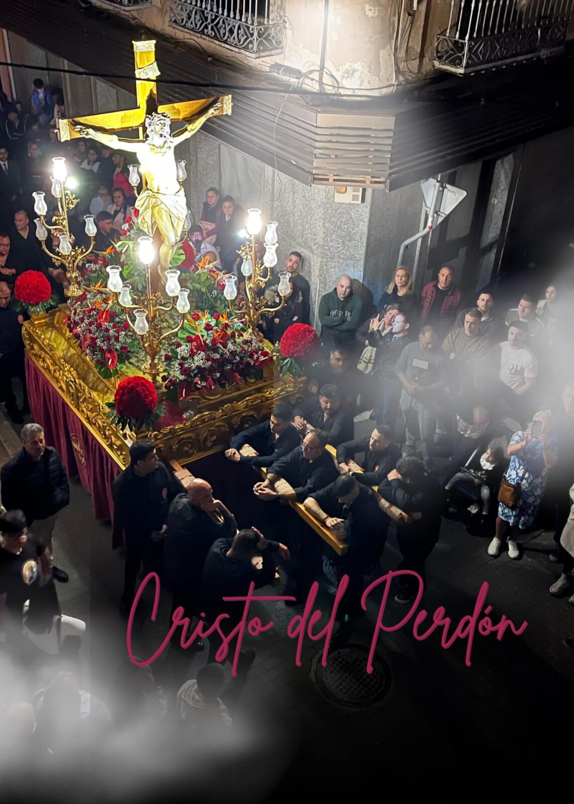 Trono del Cristo del Perdón en procesión nocturna por las calles de Fortuna, visto desde arriba con costaleros en negro y público alrededor.